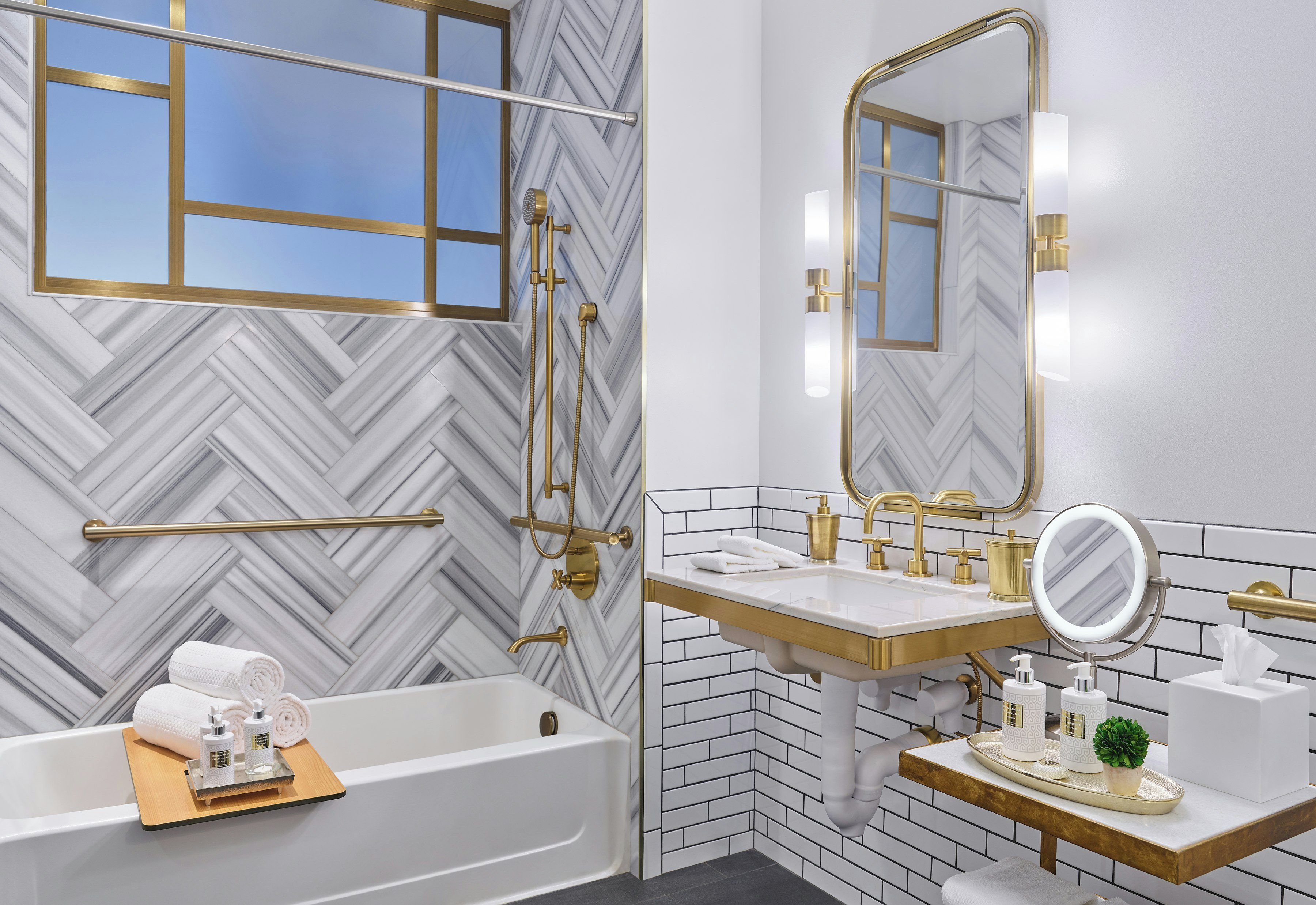 Un baño moderno con pared de diseño en patrón de espiga, una bañera independiente, un tocador con detalles dorados y un espejo con iluminación integrada.