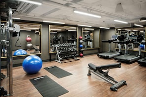 Een fitnessruimte met trainingsapparatuur, spiegels en een houten vloer.