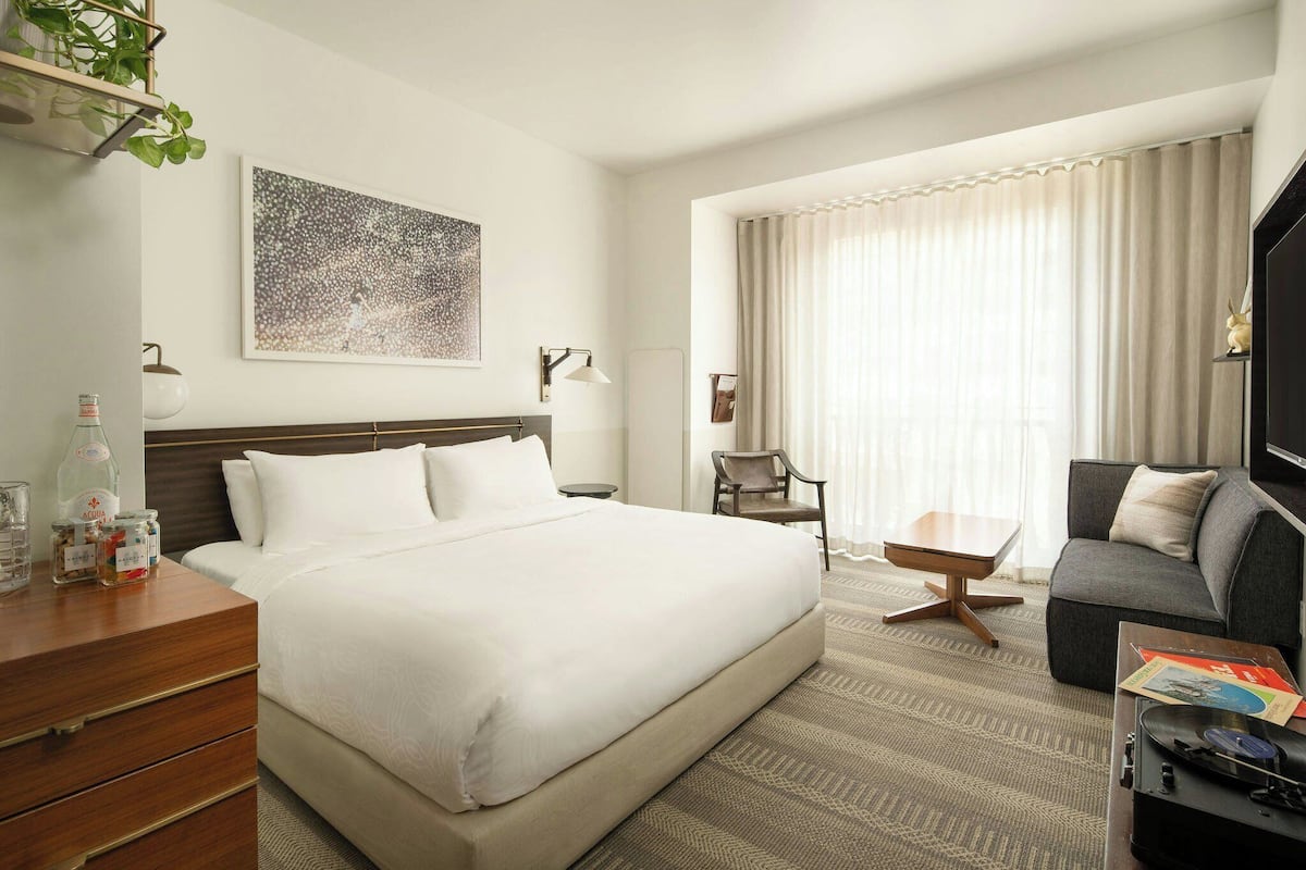 A hotel room with a large bed, a sofa, a small table, a TV, and a window with curtains.