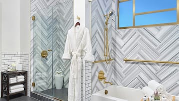Un baño moderno con pared de patrón estampilla de espiga, ducha con cerramiento de vidrio, bañera blanca y tocador de madera con toallas.