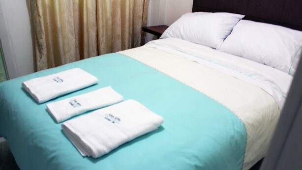 A neatly made bed with a teal bedspread and white pillows, accompanied by three folded white towels on the bed. - Hotel Casa Victoria Av 30 (Bogotá)