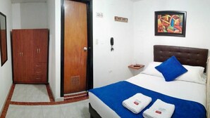 A hotel room with a bed, a wooden wardrobe, a door, a painting on the wall, and a telephone on the nightstand. - Hotel Casa Victoria Av 30 (Bogotá)
