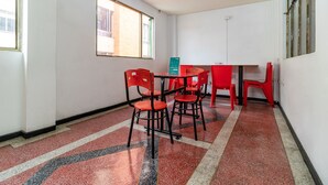A room with a red and black speckled floor, a table with chairs, and a window with a view of a building. - Hotel Casa Victoria Av 30 (Bogotá)