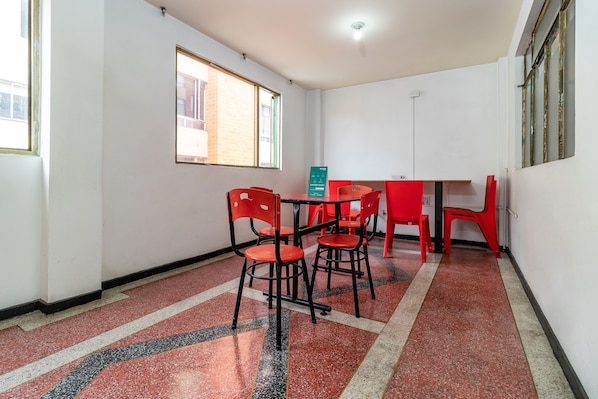 Una habitación con piso rojo y negro moteado, una mesa con sillas y una ventana con vista a un edificio.