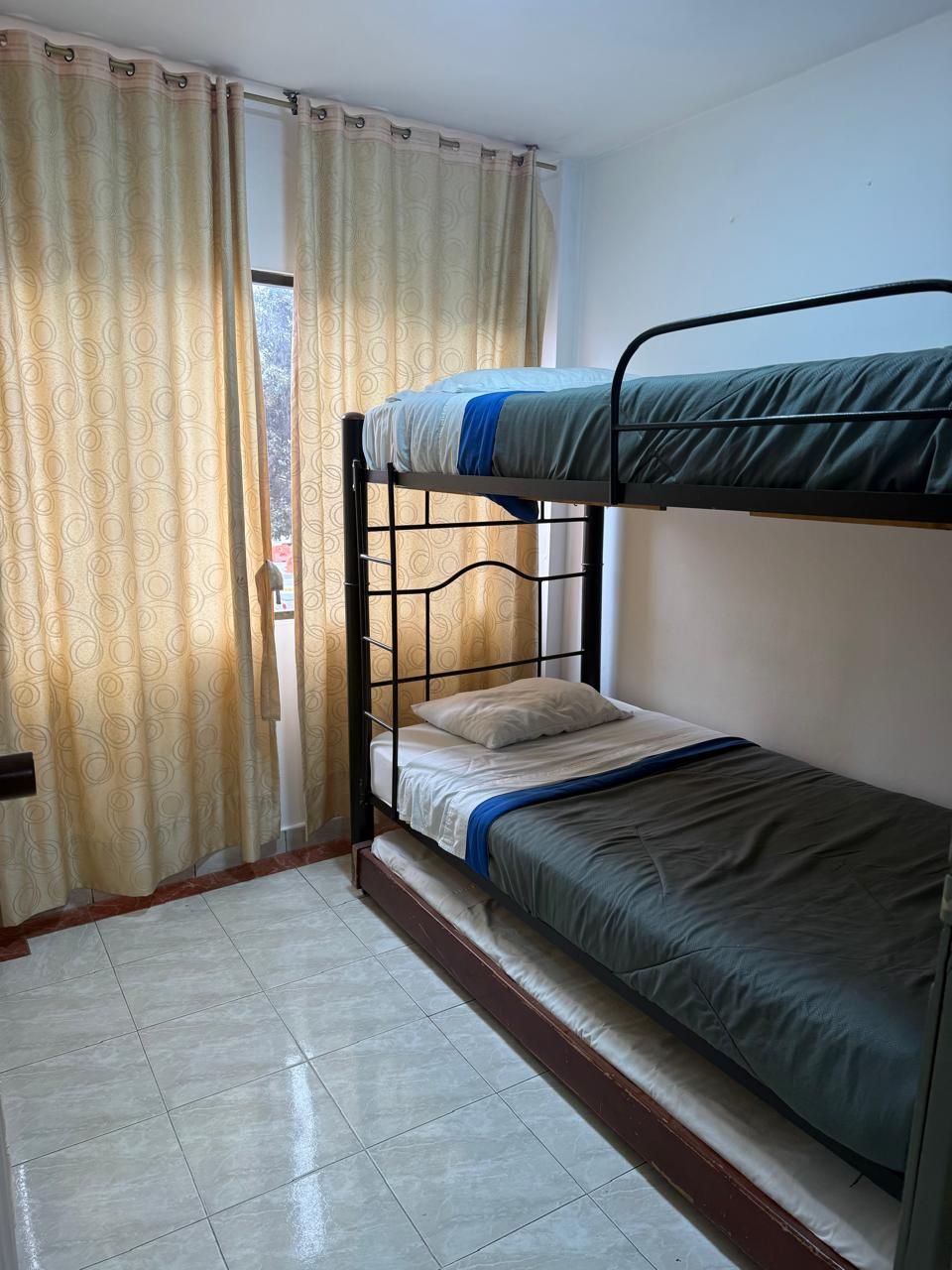Habitación con literas, cortinas, una ventana y suelo de baldosas.
