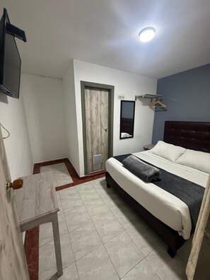 A hotel room with a bed, a TV, a mirror, and a door. - Hotel Casa Victoria Av 30 (Bogotá)