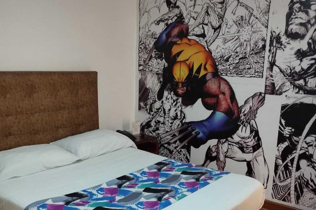 Une chambre à coucher avec un lit, une couverture colorée et un mur décoré d’œuvres d’art dans le style des bandes dessinées.