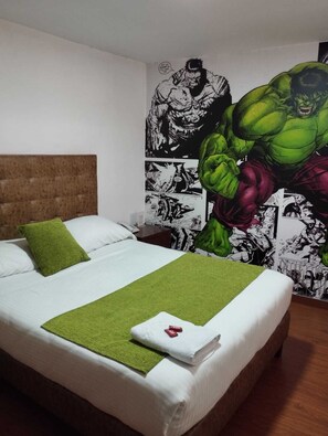 A hotel room with a large bed, green pillows, a green throw blanket, and a wall mural featuring a green muscular character. - Hotel Comic City (Bogotá)
