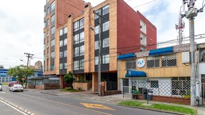 A multi-story building with a mix of brick and glass facades, a visible entrance, and a small outdoor seating area. - Hotel Comic City (Bogotá)