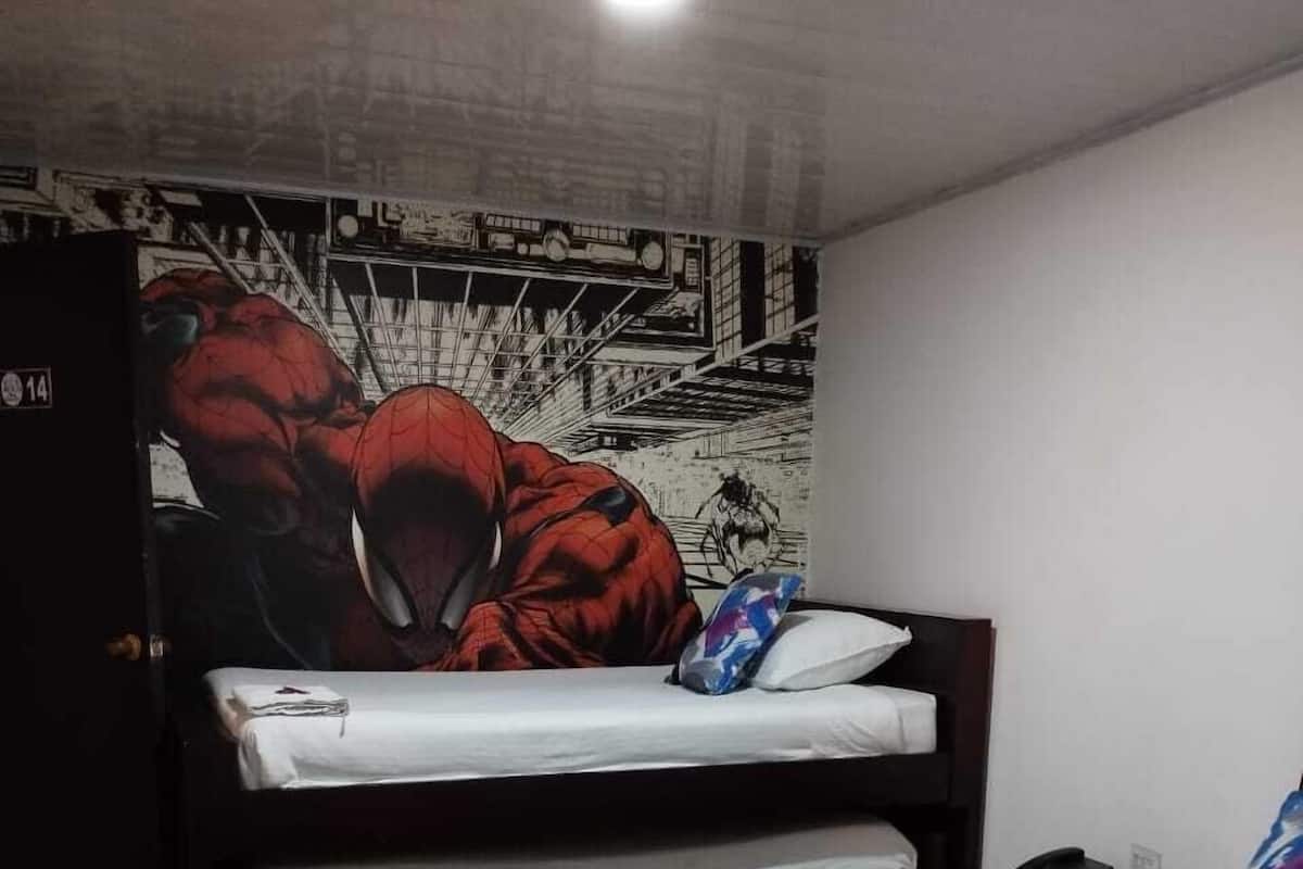 Une chambre avec un lit superposé et un lit simple, tous deux dotés de draps blancs. Un mur est décoré d’une fresque représentant un personnage de super-héros.