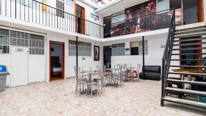 A spacious indoor area with a tiled floor, multiple tables and chairs, a staircase, and a balcony with a cityscape view. - Hotel Comic City (Bogotá)