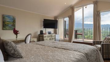 Un dormitorio con una cama grande, un televisor montado en la pared, un escritorio con una computadora y vistas a montañas a través de amplios ventanales.