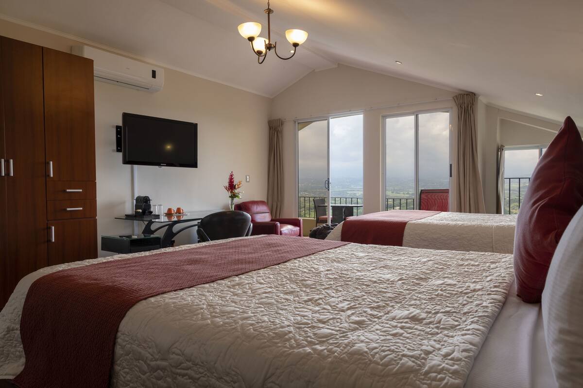 Habitación de hotel con una cama grande, un escritorio, un televisor de pantalla plana, una silla y un balcón con vistas.