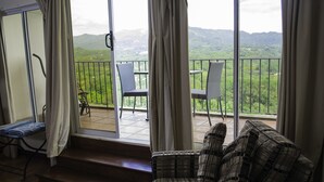 Ein Balkon mit Blick auf grüne Hügel, einer Rattan-Couch und einem Sessel.