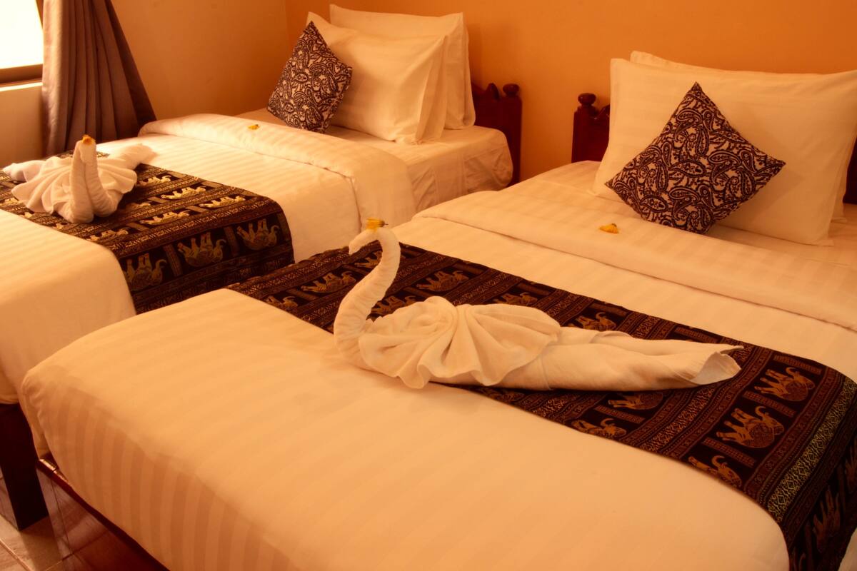 Quarto de hotel com duas camas, cada uma com lençóis brancos e almofadas estampadas.