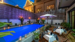 Un espace piscine avec une piscine bleue, des tables avec des parasols et des plantes en pot.