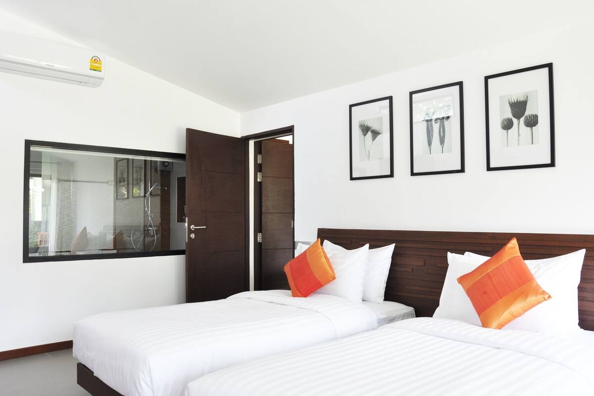 Une chambre d’hôtel avec deux lits, une grande fenêtre et trois tableaux encadrés accrochés au mur.