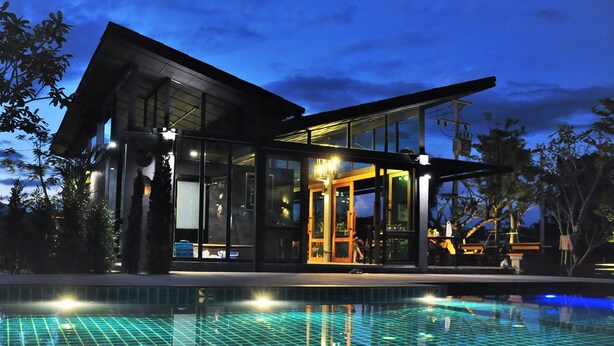 Ein modernes Haus mit großen Glasfenstern, einem Schwimmbad und einer überdachten Außenbereich.