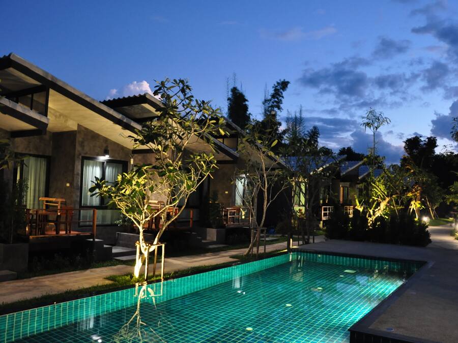 A modern hotel with a swimming pool, outdoor seating, and a well-maintained garden.