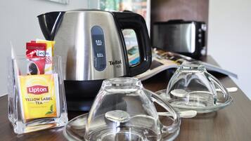A kitchen area with a stainless steel Tefal mini kettle, a Lipton Yellow Label tea packet, and two glass tea infusers on a wooden table.