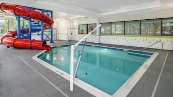 Una piscina interior con un tobogán acuático rojo y una pared con azulejos azules y blancos.