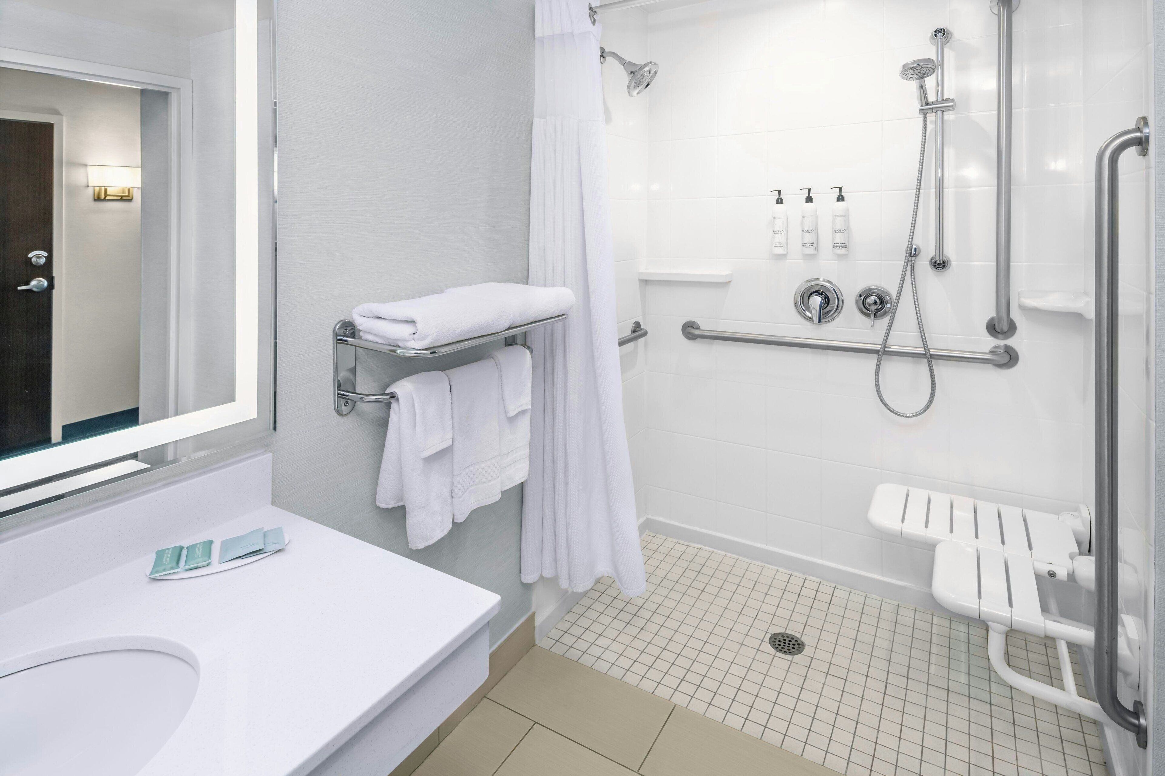 A modern bathroom with a white sink, a glass shower enclosure, a white bathtub with a grab bar, and a towel rack.
