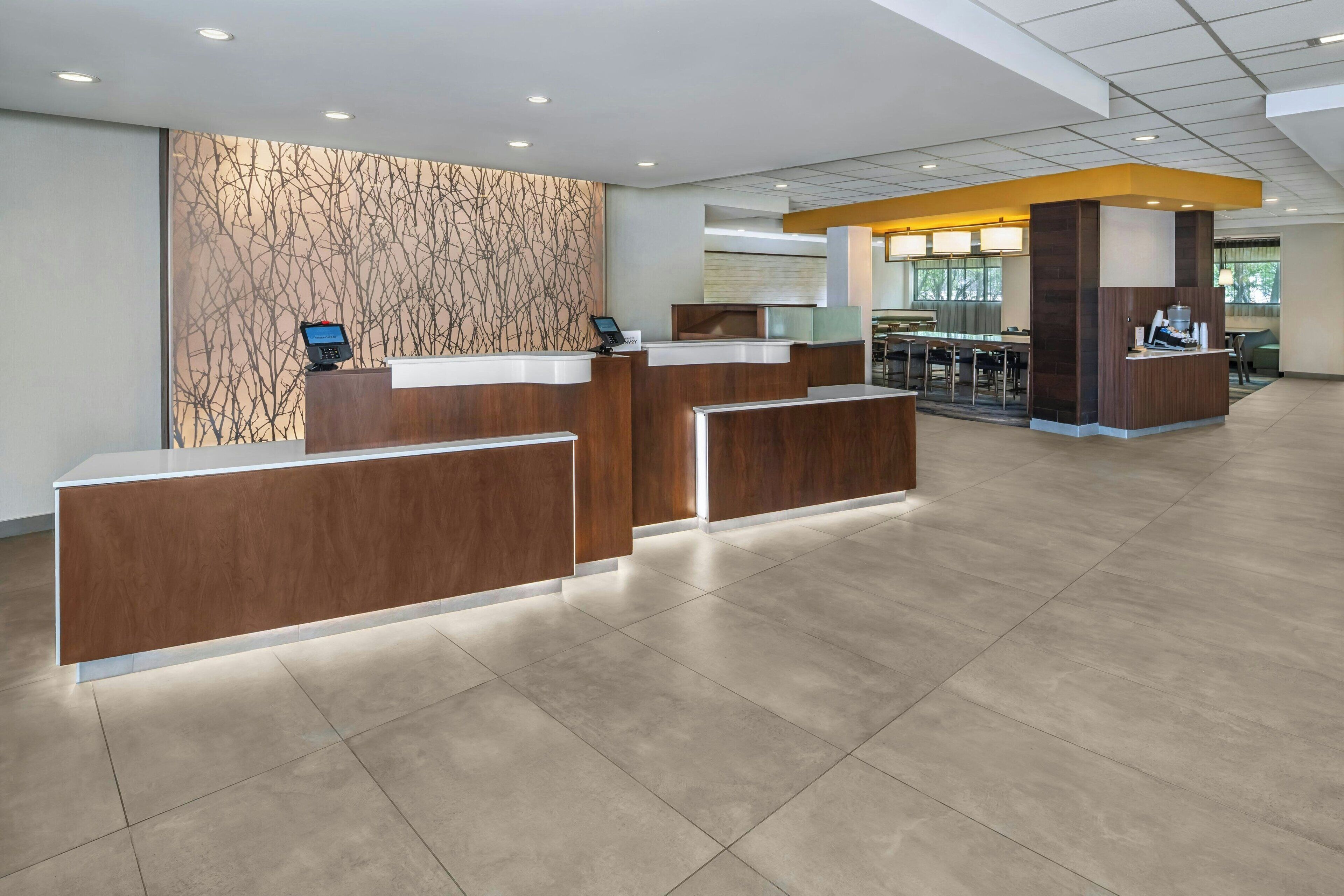 A modern hotel reception area with a wooden reception desk, a patterned wall, and a seating area with tables and chairs.