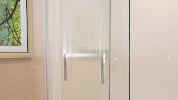 Une cabine de douche fermée par des parois de verre, avec un mur recouvert de carreaux blancs et un tableau encadré au-dessus.