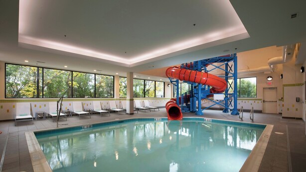 An indoor swimming pool with a red slide, sunlit windows, and lounge chairs. - Fairfield Inn & Suites by Marriott Edmonton North (Edmonton)