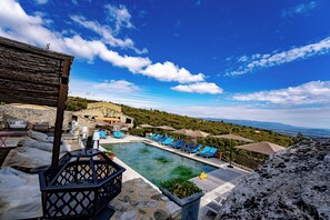 A pool area with lounge chairs and umbrellas, a stone building, and a view of the landscape.
