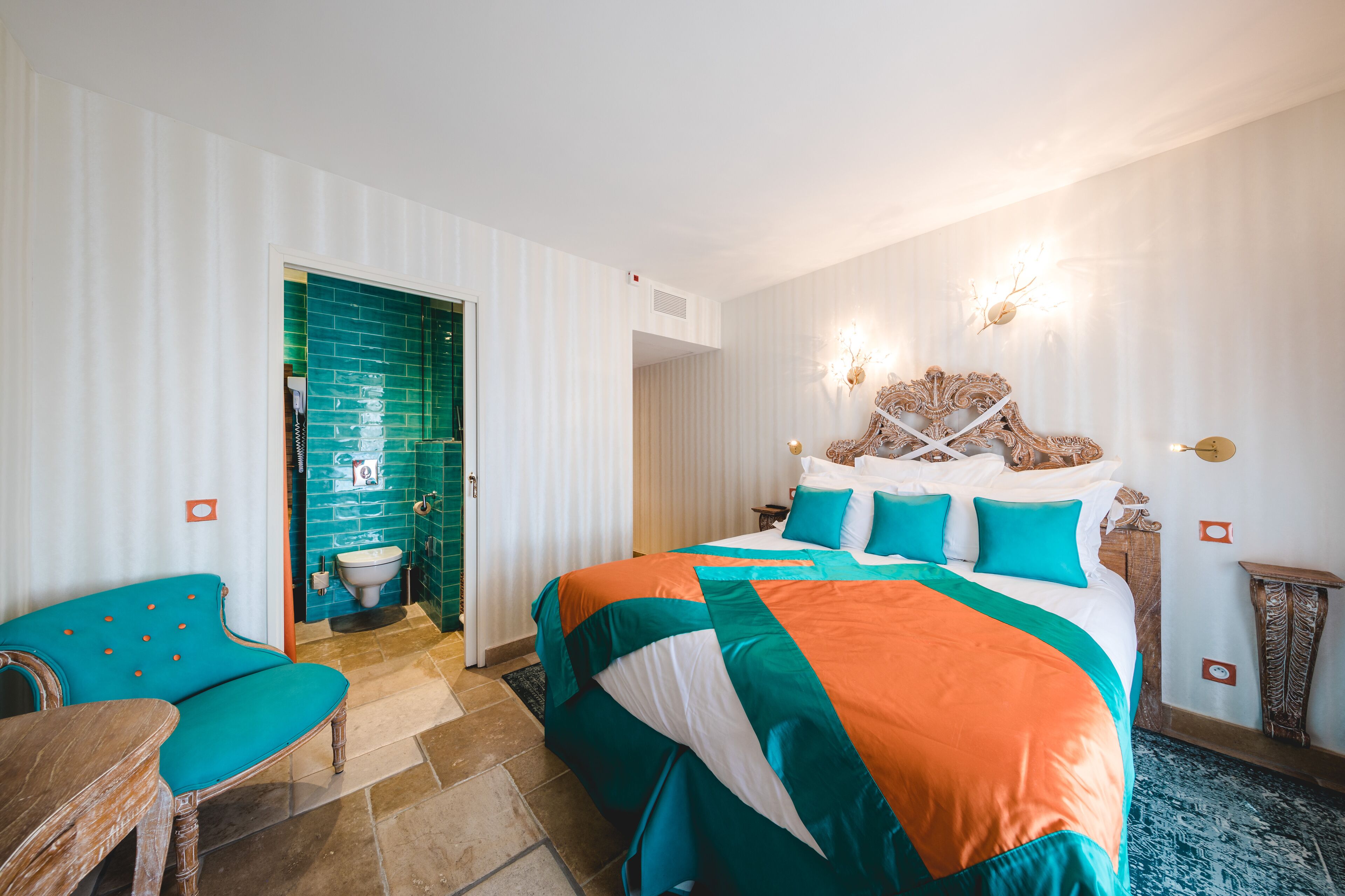 A hotel room with a large bed, a wooden chair, a bathroom with a green wall, and a patterned rug.