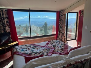 A bedroom with a large window, a bed with floral bedding, and a red chair.