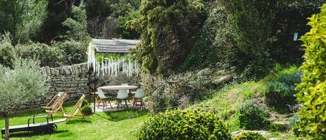 Un jardín con un muro de piedra, una pérgola de madera y una mesa con sillas.