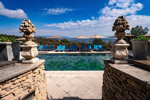 A pool area with clear water, stone walls, and blue lounge chairs. - Le Palais D'Aglaé (Gordes)
