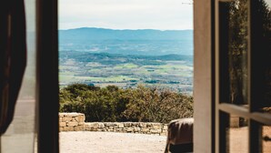 A view through an open door to a patio with a chair, a stone wall, and a landscape of hills and trees.