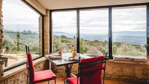 A dining area with a table set for two, large windows offering a view of the countryside.