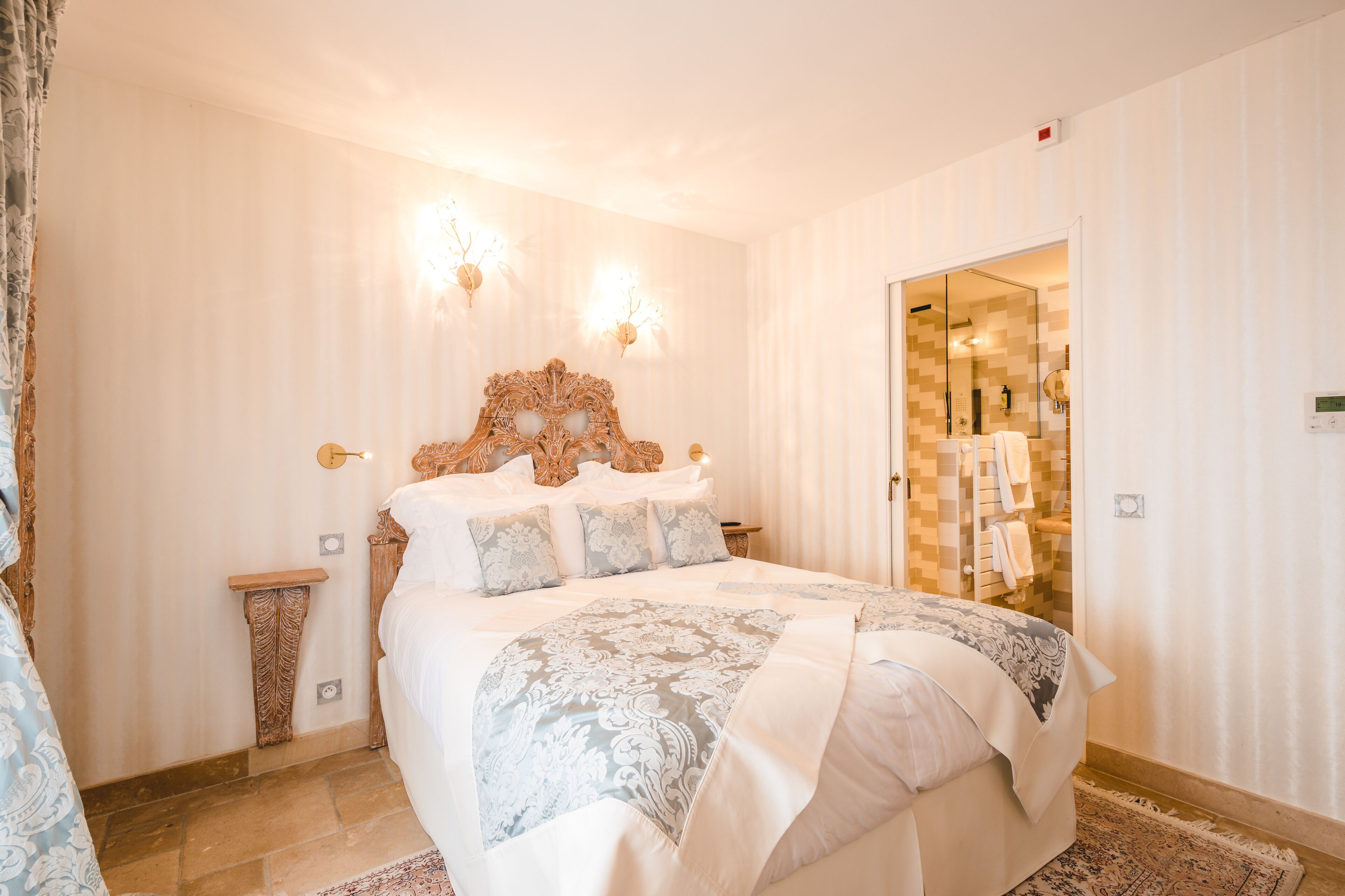 Une chambre à coucher avec un grand lit, une tête de lit en bois, deux lampes fixées au mur, une table de chevet et un miroir.