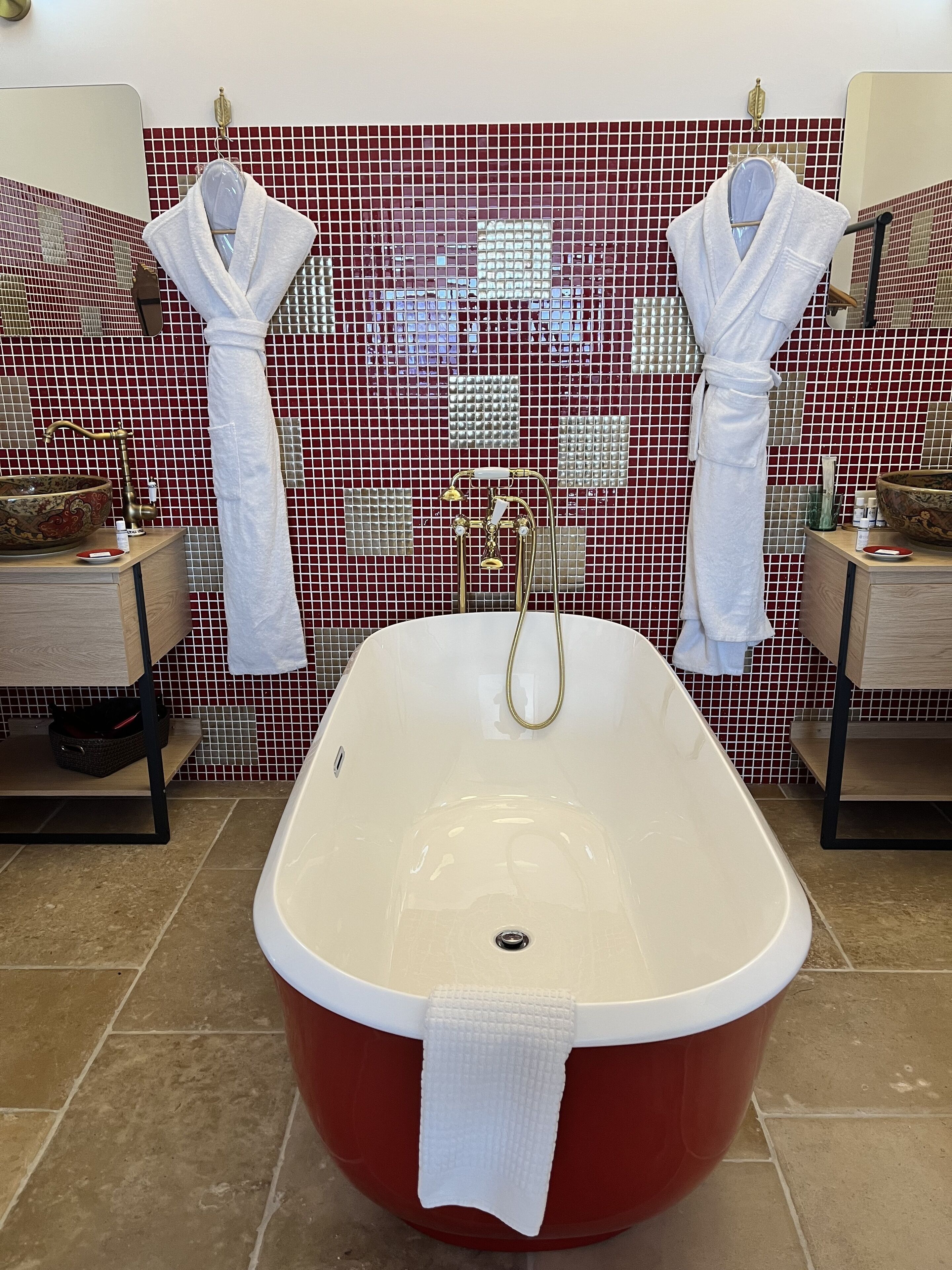 Un baño con una bañera independiente, dos toalleros con toallas blancas, un mueble de tocador de madera y un salpicadero de azulejos.