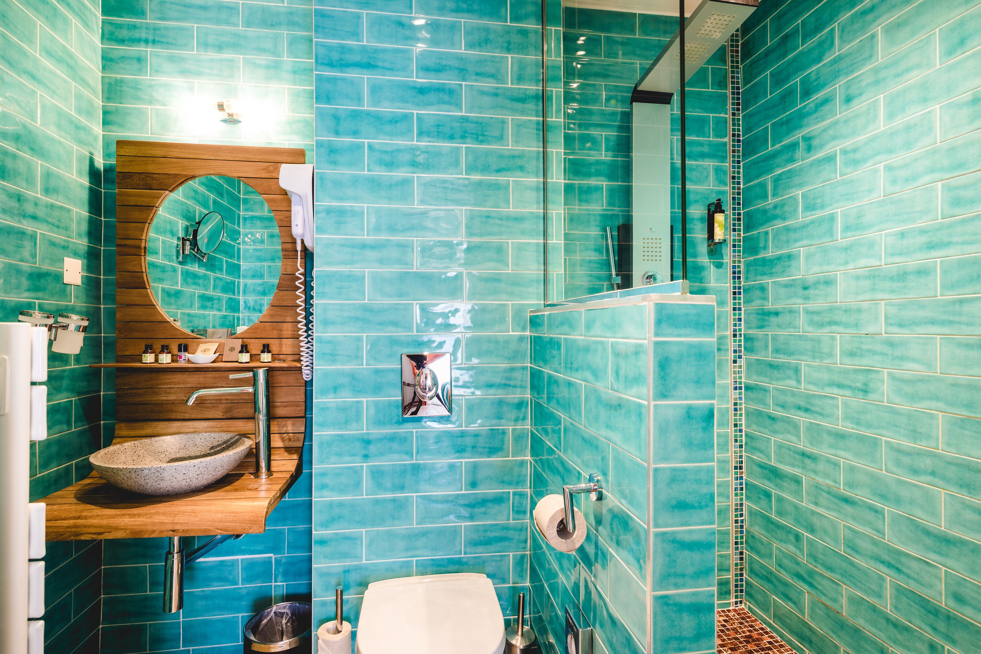 A bathroom with a round mirror, a wooden vanity, a sink, and a toilet.