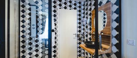 A modern bathroom with a geometric patterned wall, a glass shower enclosure, a wooden vanity, and a large mirror.