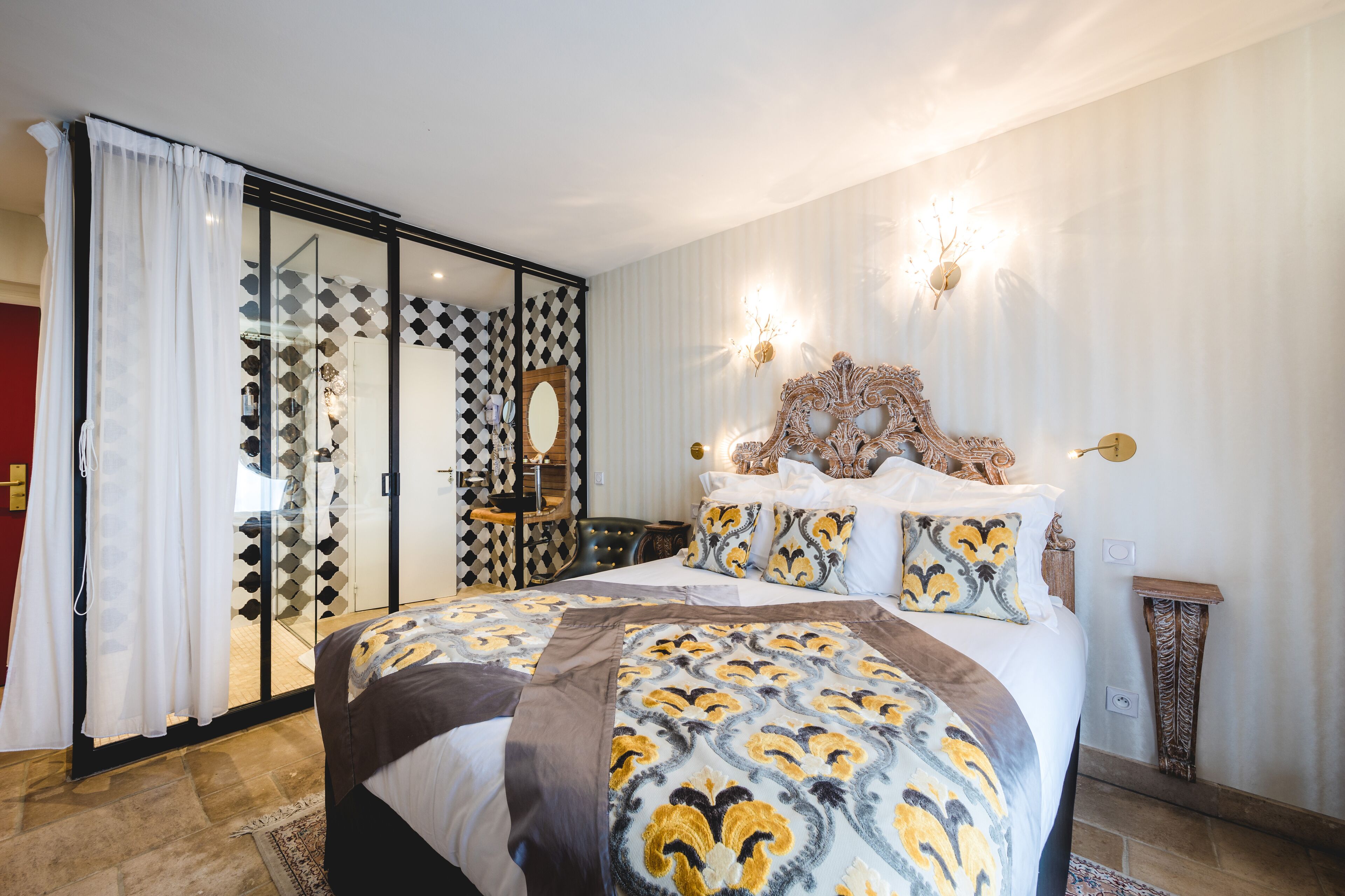 Een slaapkamer met een groot bed, een schuifdeur met glas, een spiegel en decoratieve wandlampen.
