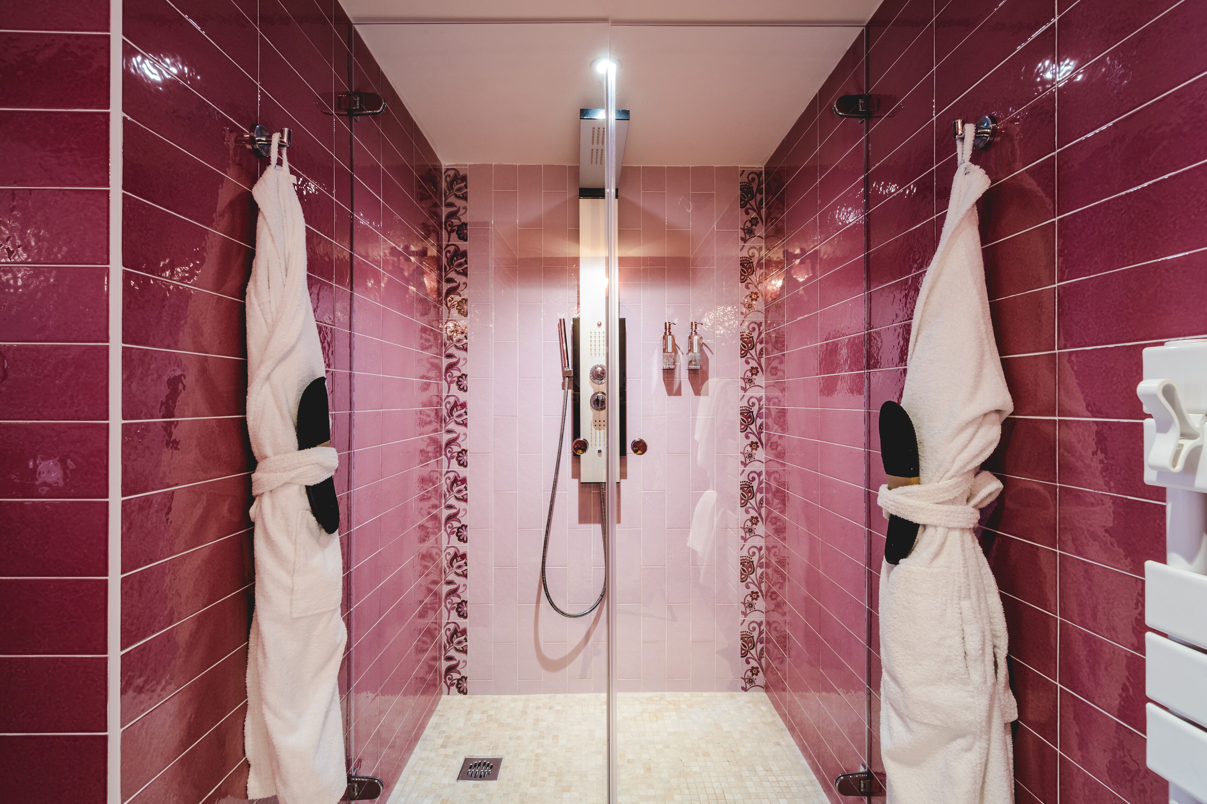 A walk-in shower with a glass door, pink tiled walls, and two white towels hanging on hooks.
