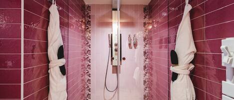 A walk-in shower with a glass door, pink tiled walls, and two white towels hanging on hooks.