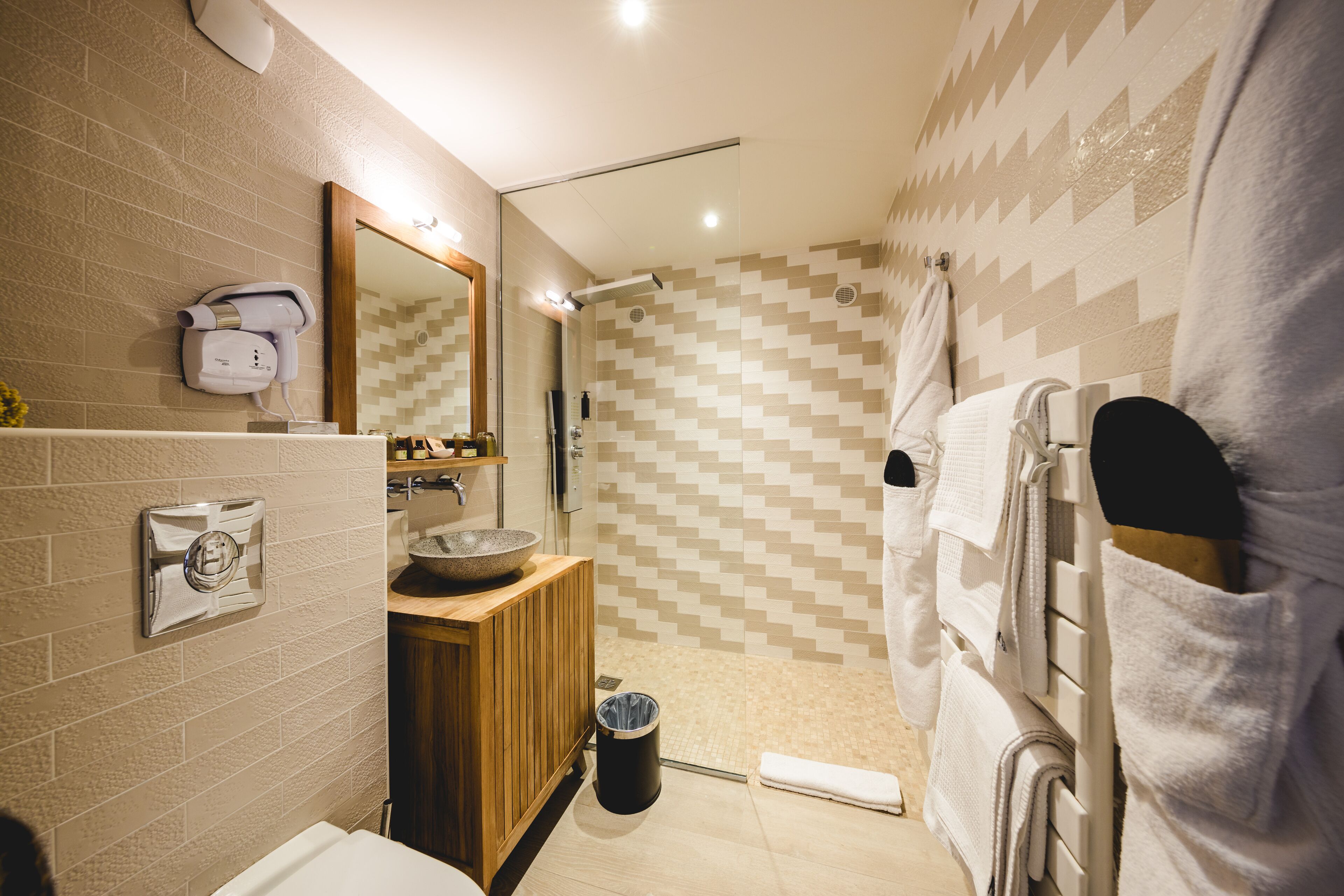 Un baño moderno con tocador de madera, lavamanos integrado, espejo y zona de ducha con azulejos estampados.