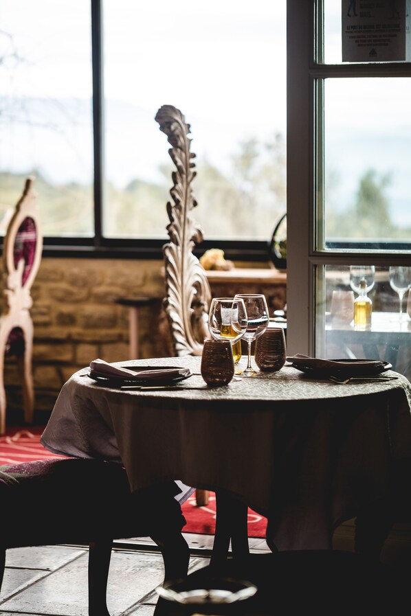 A dining table with wine glasses and a bottle, set against a window with a view of trees. - Le Palais D'Aglaé (Gordes)