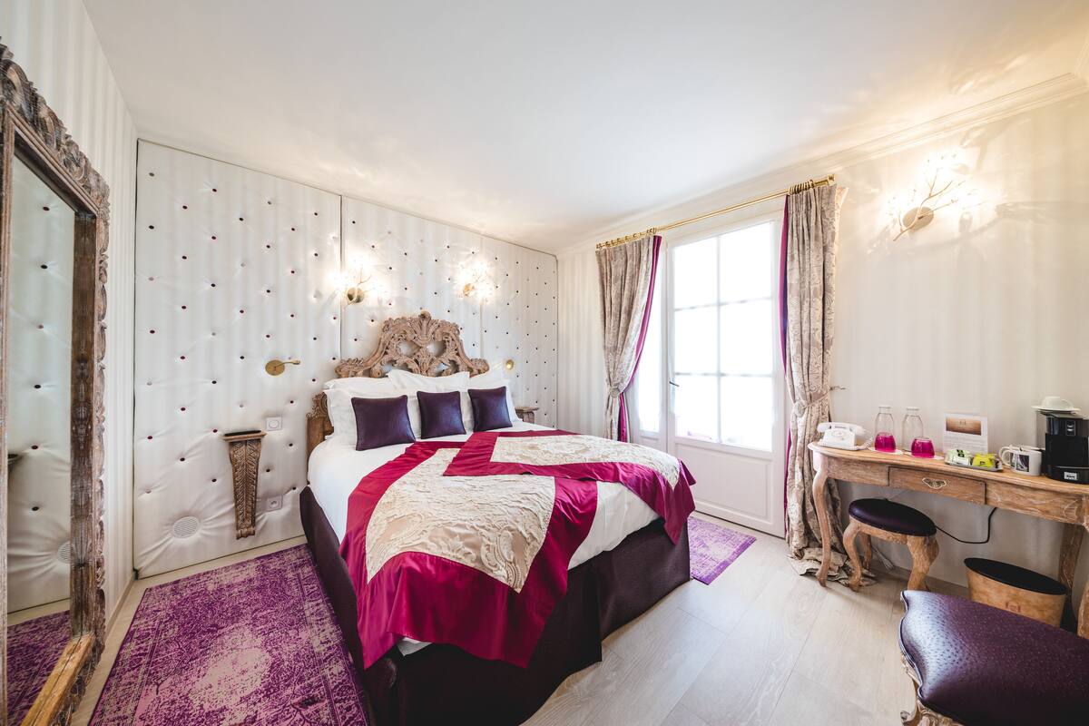 Une chambre avec un grand lit, un bureau avec une chaise et une fenêtre avec des rideaux.