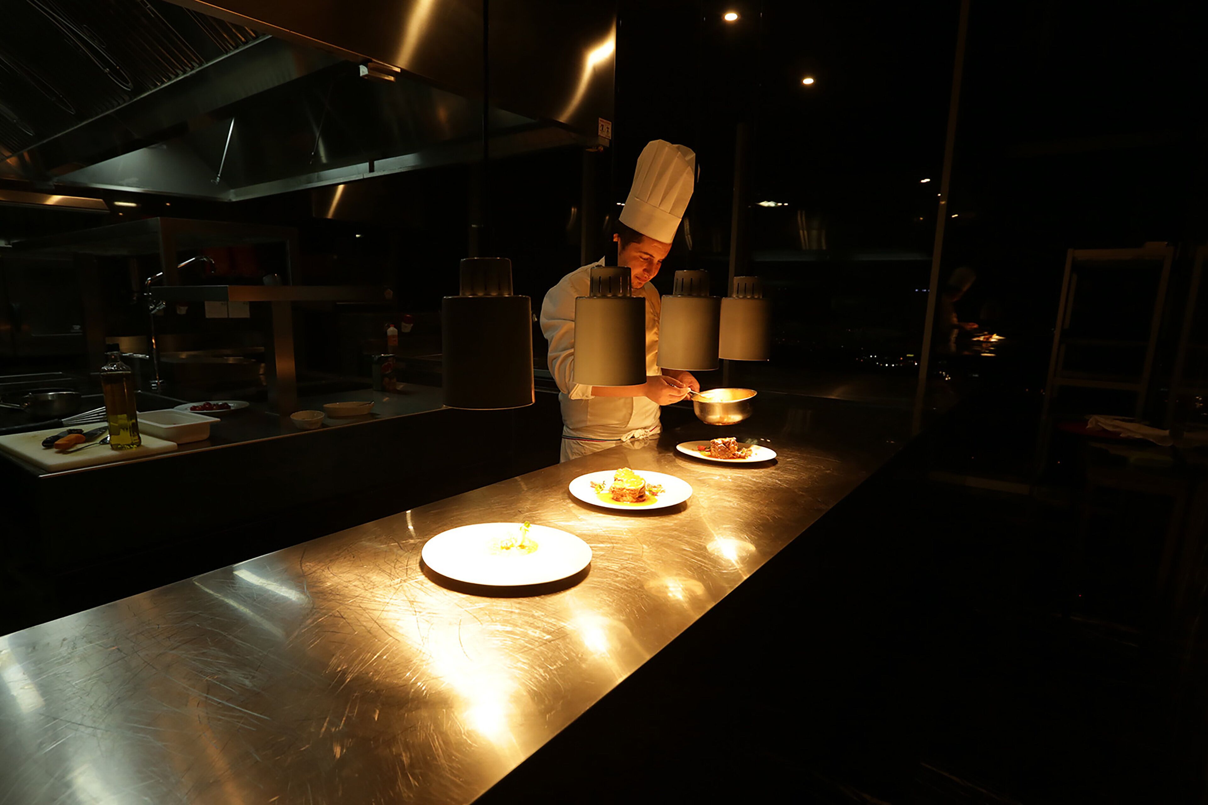 Un chef preparando comida en una cocina luminosa con superficies de acero inoxidable y equipo moderno.