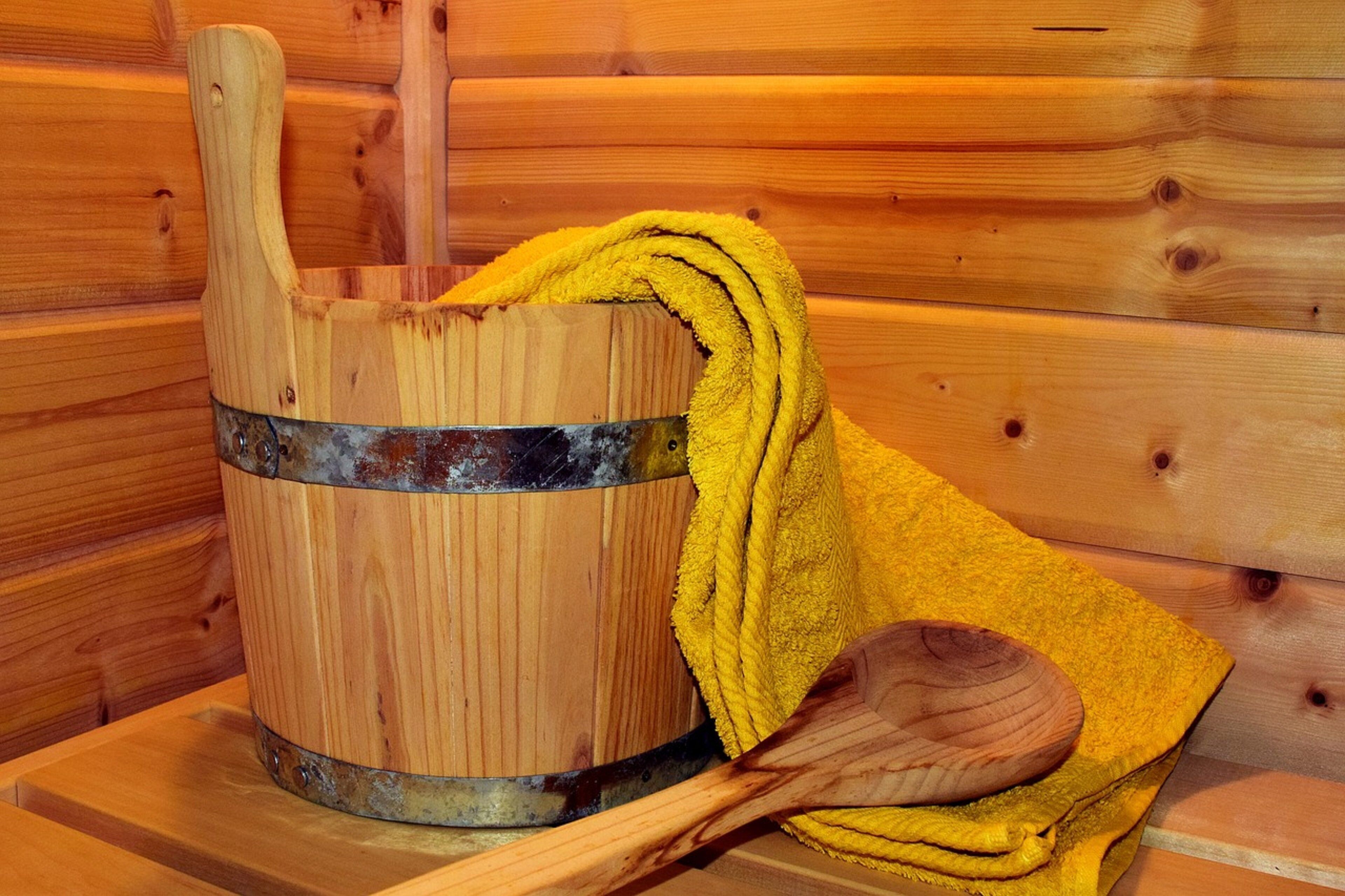 A wooden bucket with a metal band, a yellow towel, and a wooden spoon on a wooden surface.