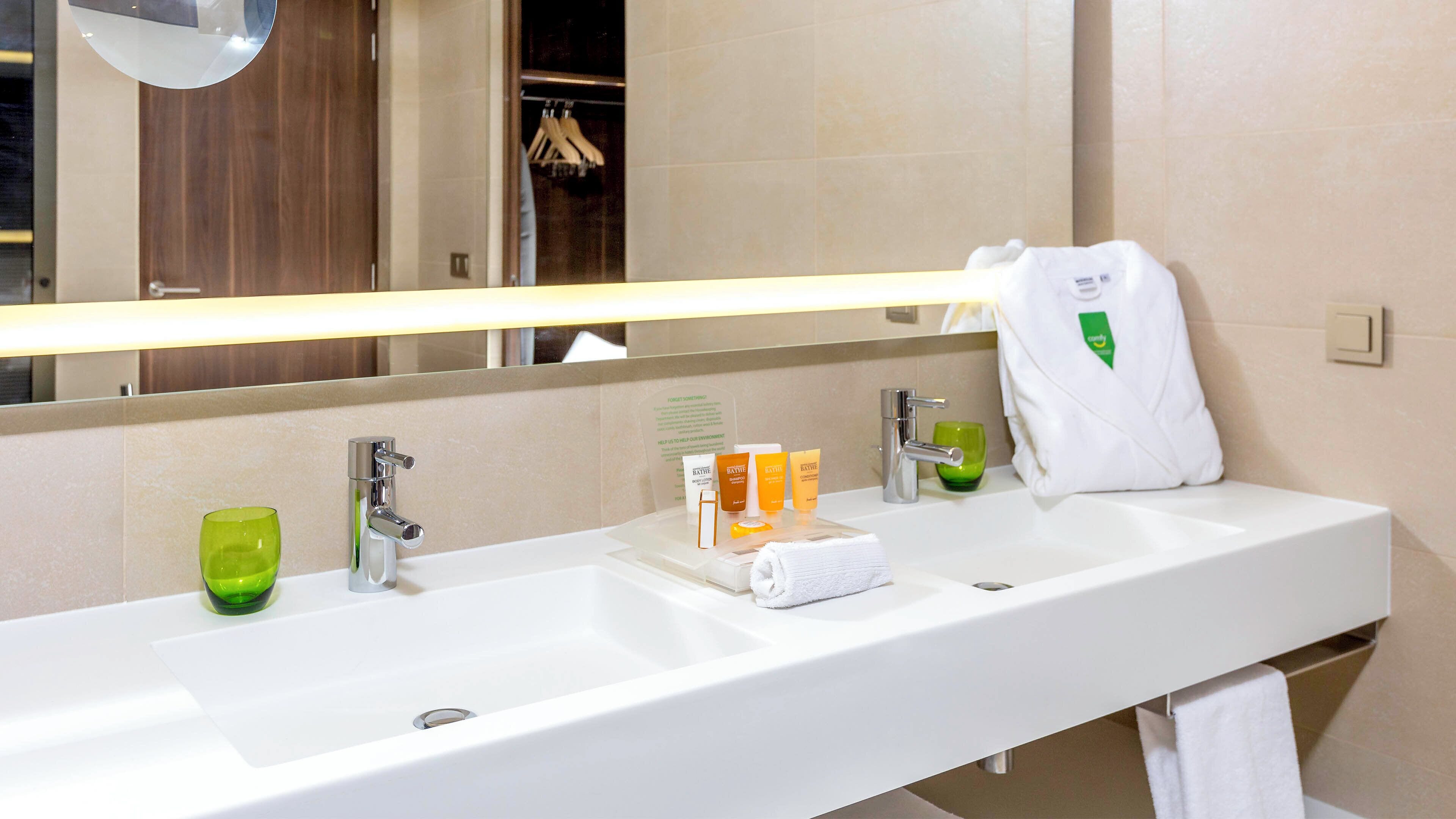 Un bany d'hotel amb un mirall gran, dues dutxes, un escurapulides i productes de tocador.