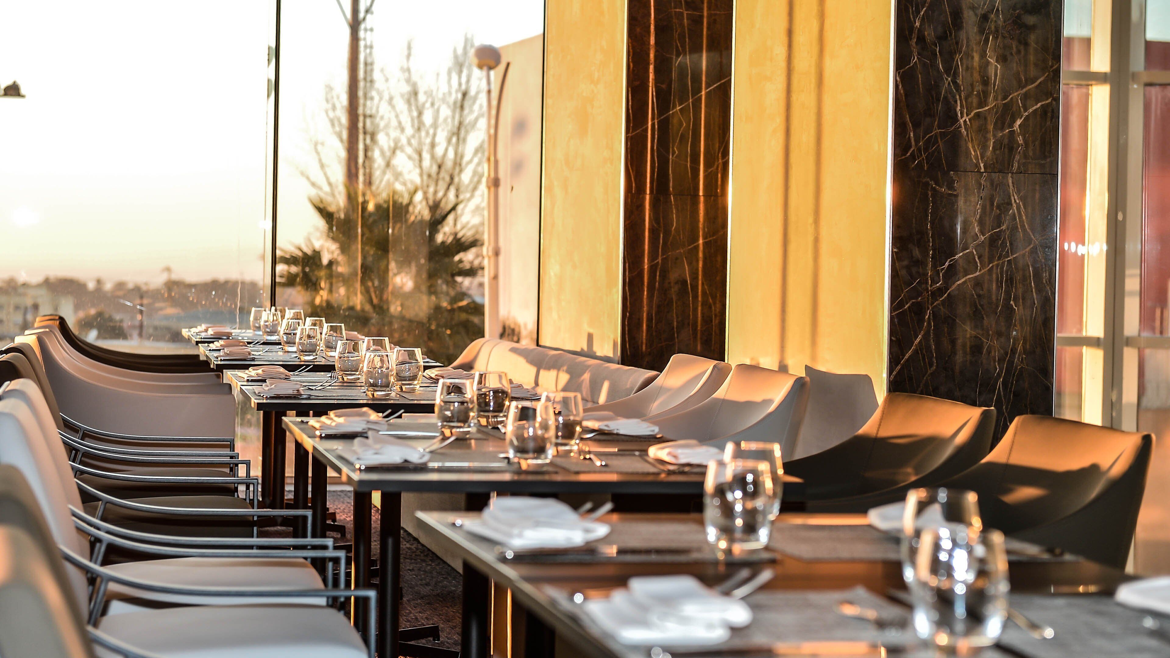 A restaurant with a long table set for a meal, chairs, and a view of the cityscape.